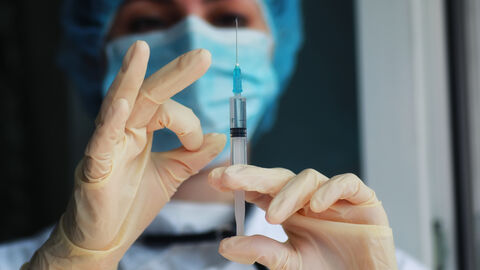 Ärztin mit Handschuhen und Maske, die eine Spritze aufzieht Ärztin mit Handschuhen und Maske, die eine Spritze aufzieht