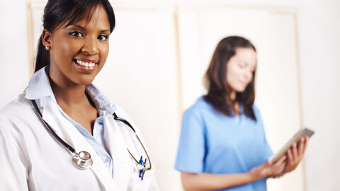 Ärztin mit einer Mitarbeiterin mit einem Tablet-PC im Hintergrund