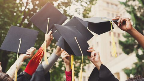Feierende Studenten nach Zeugnisübergabe Eine Gruppe multiethnischer Studenten, die ihren Abschluss feiern, indem sie Mützen in die Luft werfen.