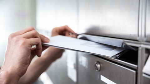 Hand einer Person, die Briefe in den Briefkasten einwirft Hand einer Person, die Briefe in den Briefkasten einwirft
