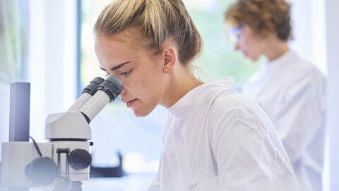Junge Frau schaut durch Mikroskop
